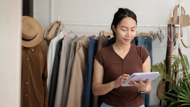 Asian woman using tablet to manage orders and inventory in home fashion shop