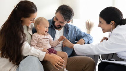 Female doctor playing comforting infant baby sitting on parents lap