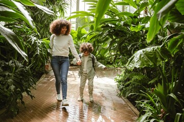 A mother and her son walk among the plants and smile while holding hands
