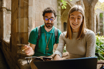 A man is looking at a notebook and talking to a woman who is sitting next to him and smiling while...