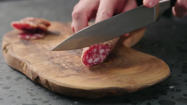 Slow motion man slicing fuet sausage on olive wood board