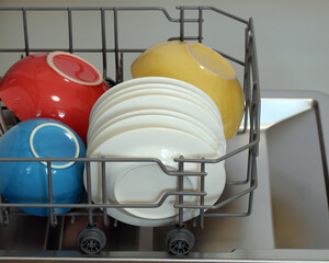 Loading dirty dishes and colorful bowls into dishwasher