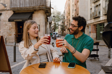 A man and a woman are talking and raising their glasses while sitting at a table