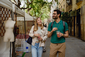 A man and a woman walk and hold cups while smiling