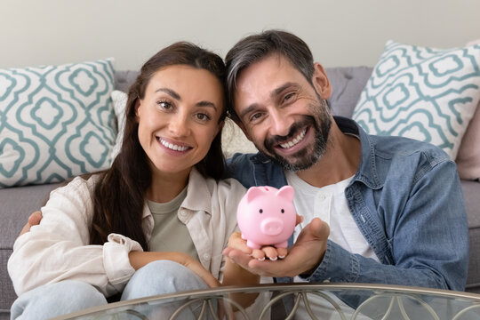Portrait happy married couple hugging looking at camera holding piggybank