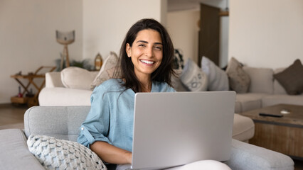 Naklejka premium Cheerful beautiful young Latin woman using laptop at home