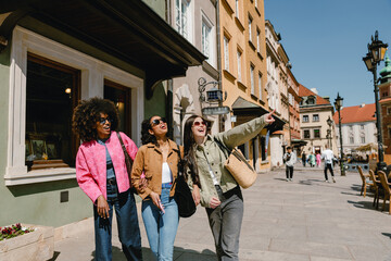 Fototapeta premium A group of three female friends holding hands and laughing as they walk and look in the direction one of them is pointing