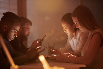 Multiethnic group of white collar workers checking social media on their gadgets while sitting in break room in the evening