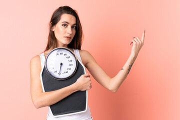 Young woman over isolated pink background with weighing machine and doing victory gesture