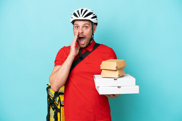 Young caucasian man with thermal backpack and holding fast food isolated on blue background with surprise and shocked facial expression