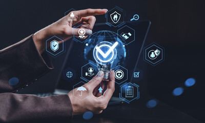 Businessperson holding glowing lightbulb with digital checkmark hologram surrounded by futuristic icons representing trust and data protection concept.
