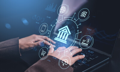 Digital banking concept with hologram icons of financial services and fintech technology displayed above hands typing on laptop keyboard in dim light.