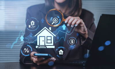Real estate investment analysis concept with businesswoman using smartphone and magnifying glass over digital hologram of house on blue background.