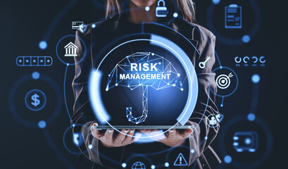 Businesswoman holding tablet with glowing hologram umbrella labeled risk management surrounded by finance and security icons on dark background concept..