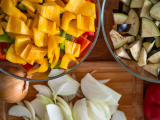 Fresh chopped vegetables: white onion, colorful bell peppers, eggplant on wooden table. Top view