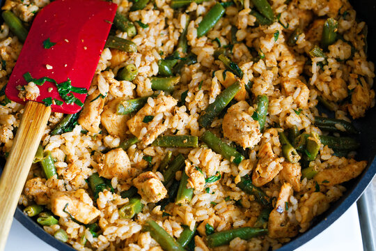 Closeup pieces of chicken meat and vegetables like rice and green beans are fried in a pan. Shallow focus.
