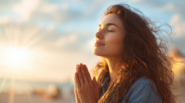 A woman with long hair is praying in the sun. She is smiling and looking up at the sky