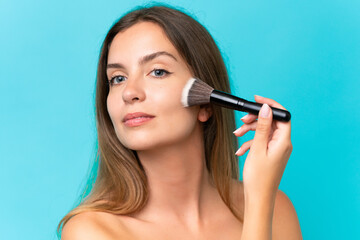 Fototapeta premium Young caucasian woman isolated on blue background holding makeup brush