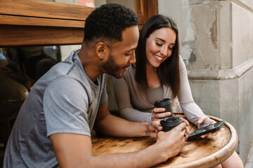 Male and female athletes sitting at a table holding cups while looking at the phone she is holding...