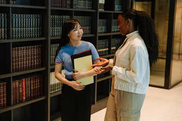 Two female students walking and talking while one of them carries a folder and a notebook