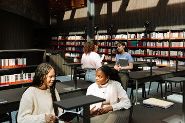 Two female students are talking and sitting at a table while two other female students are standing...