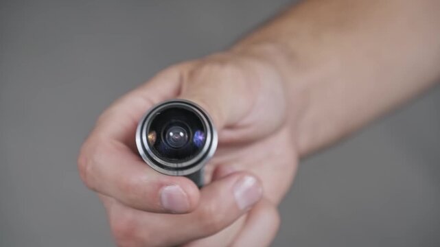 Macro view of a hand holding a compact peephole camera. Focus is on the convex fisheye lens highlighting optical details of modern home security and surveillance equipment.