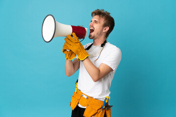 Young electrician man over isolated wall shouting through a megaphone
