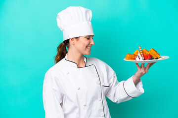 Young caucasian chef woman holding waffles isolated on blue background with happy expression