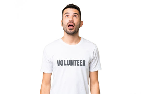 Young volunteer caucasian man over isolated chroma key background looking up and with surprised expression