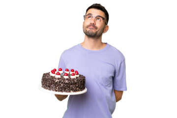 Young caucasian man holding birthday cake isolated on green chrome background and looking up