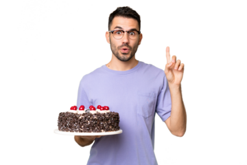 Young caucasian man holding birthday cake isolated on green chrome background intending to realizes the solution while lifting a finger up