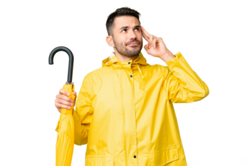 Young caucasian man with rainproof coat and umbrella over isolated background having doubts and thinking