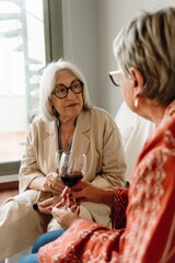 A woman listens to her female friend sitting next to her on the couch while they hold glasses