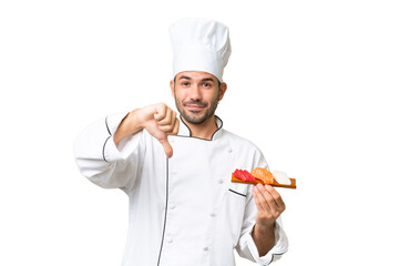 Young caucasian chef holding a sushi over isolated background showing thumb down with negative expression