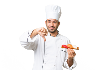 Young caucasian chef holding a sushi over isolated background showing thumb down with negative expression