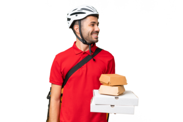 Young handsome caucasian man with thermal backpack and holding takeaway food over isolated background looking side