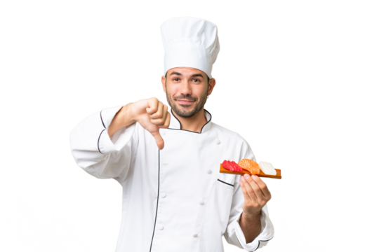 Young caucasian chef holding a sushi over isolated background showing thumb down with negative expression