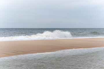 Gentle waves roll onto the empty sandy shore under a calm sky. The scene captures peaceful seaside simplicity.