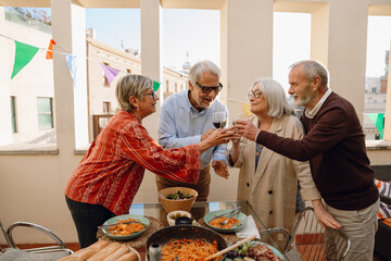 A group of four friends clink glasses and talk while standing at a table and smiling