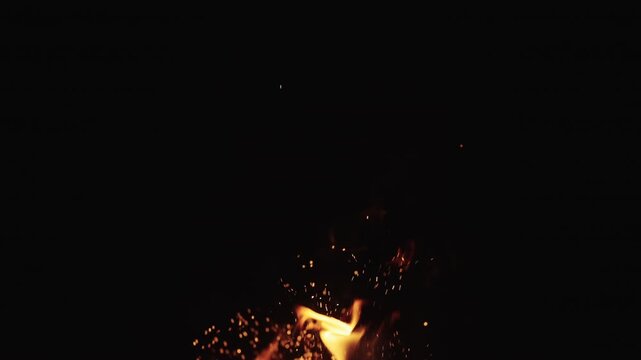 Realtime shot of fire flames with sparks rising of campfire over black background