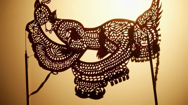 Detailed shot of an ornate shadow puppet against a backlit warm yellow-orange backdrop