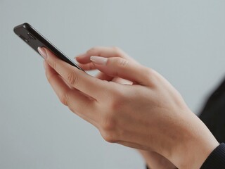 両手でスマートフォンを操作する若い女性の手元（左向き）