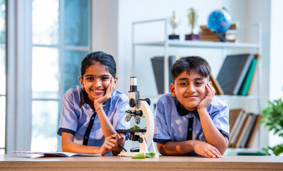 Uniformed Indian students examine plant samples under microscope and take notes in science class