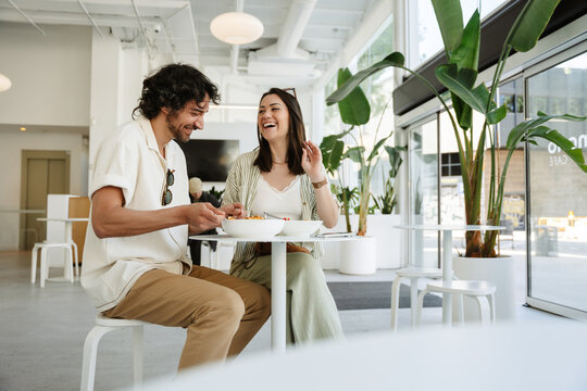 A woman and a man are laughing and sitting at a table with plates of food on it