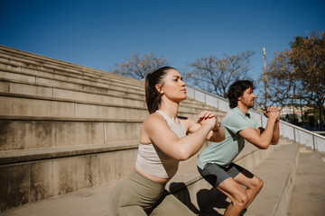 Female and male athletes squatting while holding hands together in front of them and standing on stairs