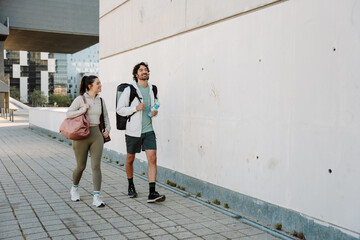 Obraz premium A man and a woman walk and smile while carrying mats, bags, and a bottle