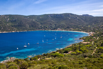 Obraz premium view of Campomoro Bay, where several boats are anchored in clear blue and turquoise water under sunshine and blue skies