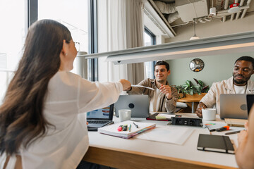 A male and female employee hold documents above a table where they sit next to two other employees