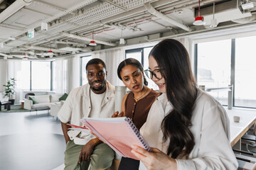 A group of three workers stand looking at a notebook that one of them is showing while two of them...