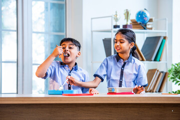 Indian students enjoy lunch break, sharing tiffin laughter in classroom wearing school uniforms